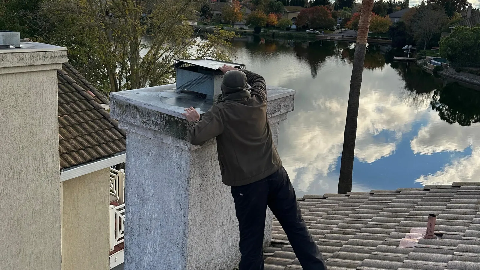 A Chimney Guys technician working a rooftop chimney above the reservoir, the water and sky behind him