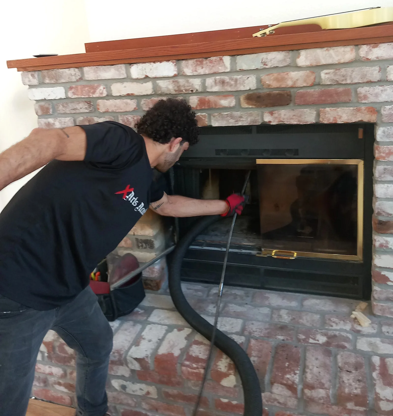 A Chimney Guys technician feeding sweeping rods into a glass-front fireplace insert